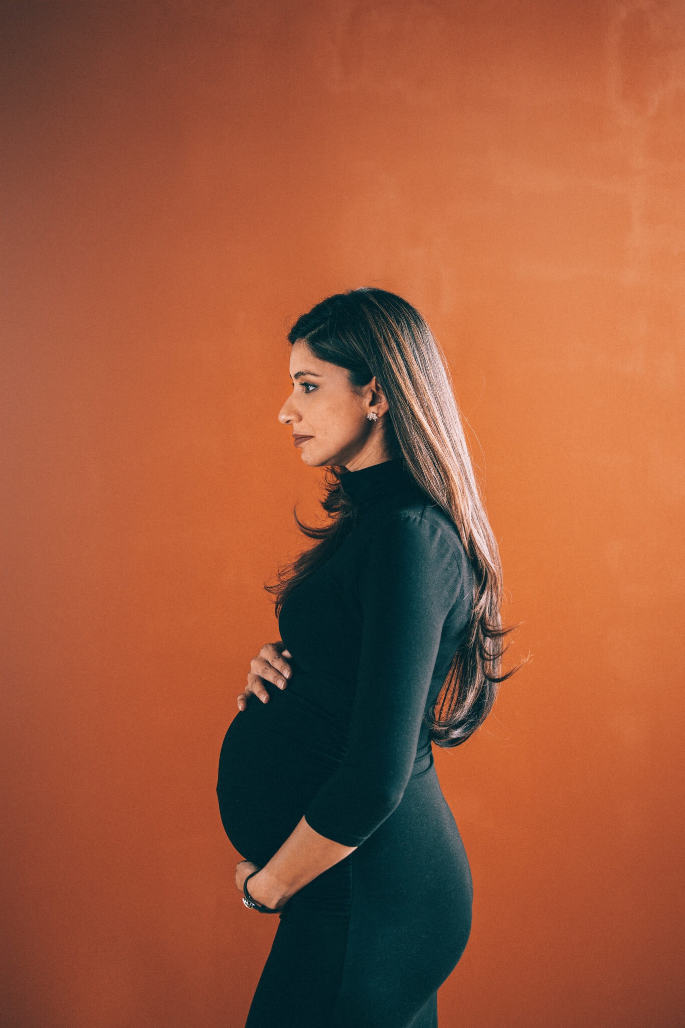 Commercial portrait photography example by Hannah Dunsirn. A side profile of a pregnant woman with an orange background.